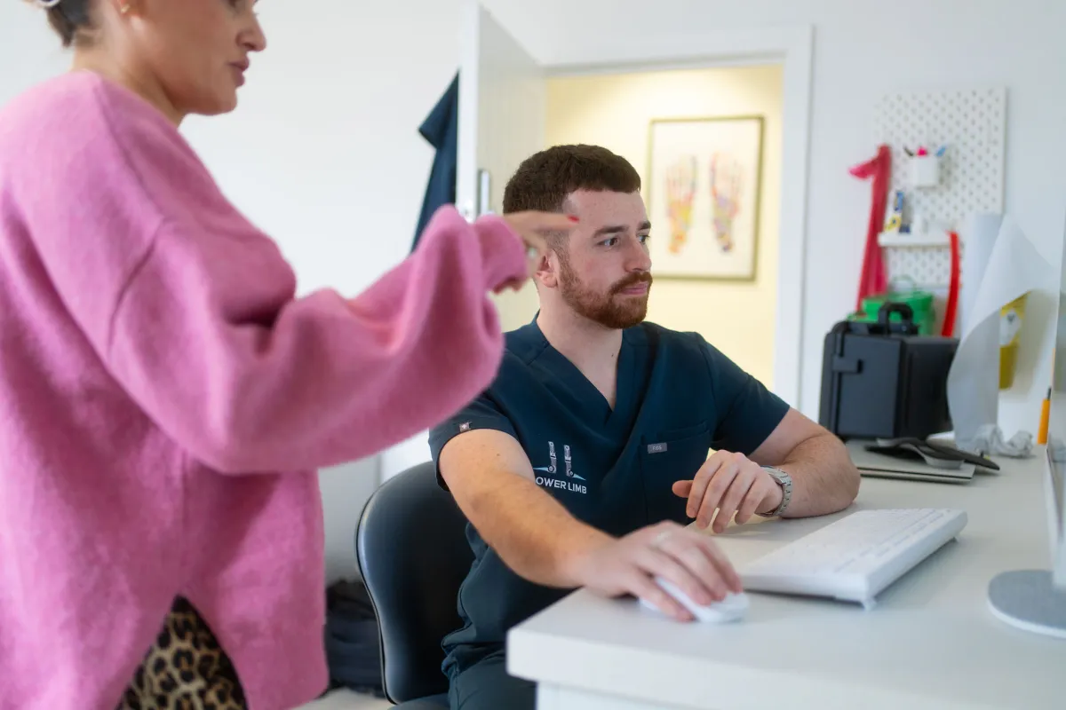 Podiatrist at desk during a consultation about foot pain from prolonged standing at Lower Limb Clinic Belfast